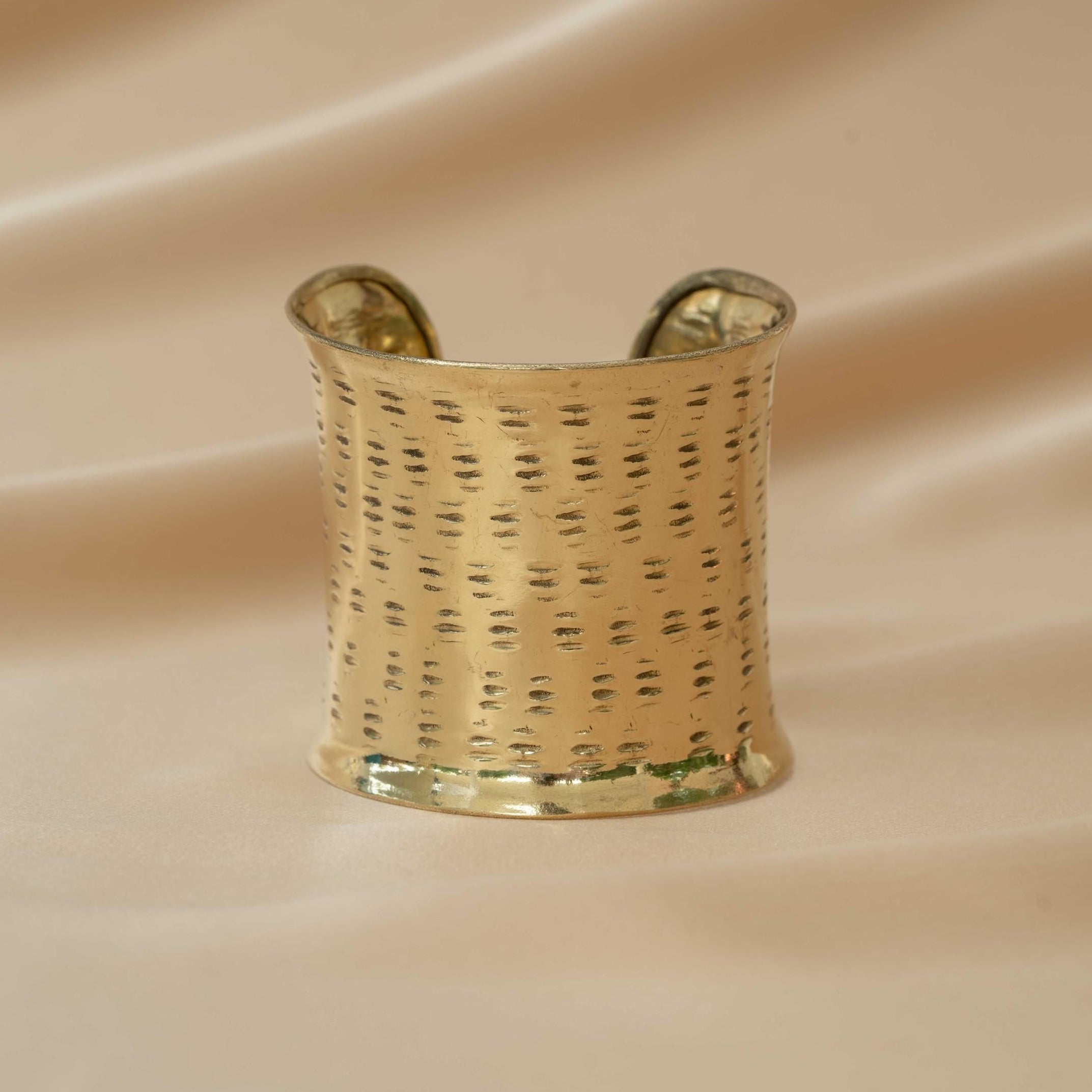 Gold bracelet cuff on a beige fabric background